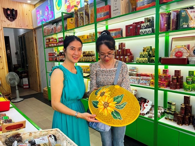Kh&aacute;ch h&agrave;ng trải nghiệm sản phẩm N&oacute;n l&aacute; vẽ hoa hướng dương tại một điểm giới thiệu v&agrave; b&aacute;n sản phẩm OCOP kết hợp với du lịch tại Huế. Việc gắn kết n&agrave;y gi&uacute;p gia tăng gi&aacute; trị văn h&oacute;a v&agrave; tạo trải nghiệm trực tiếp cho người ti&ecirc;u d&ugrave;ng. (Ảnh: CTV)