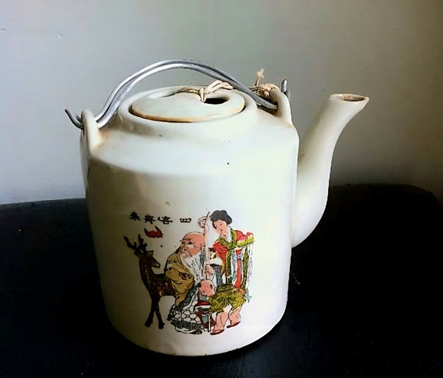 B&igrave;nh t&iacute;ch tr&agrave; từ gốm xanh pha m&agrave;u ngọc b&iacute;ch, tr&ecirc;n th&acirc;n b&igrave;nh c&oacute; hoa văn l&agrave; c&aacute;c h&igrave;nh ảnh d&acirc;n gian gi&agrave;u bản sắc