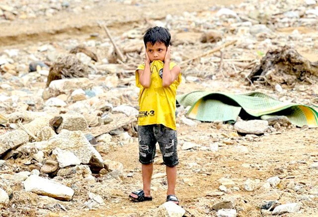 Giữa b&atilde;i đất trống, chỉ c&ograve;n lại h&igrave;nh ảnh cậu b&eacute; mặc &aacute;o v&agrave;ng chuối ch&iacute;n, đ&ocirc;i mắt buồn nh&igrave;n về nơi từng l&agrave; nh&agrave; m&igrave;nh.